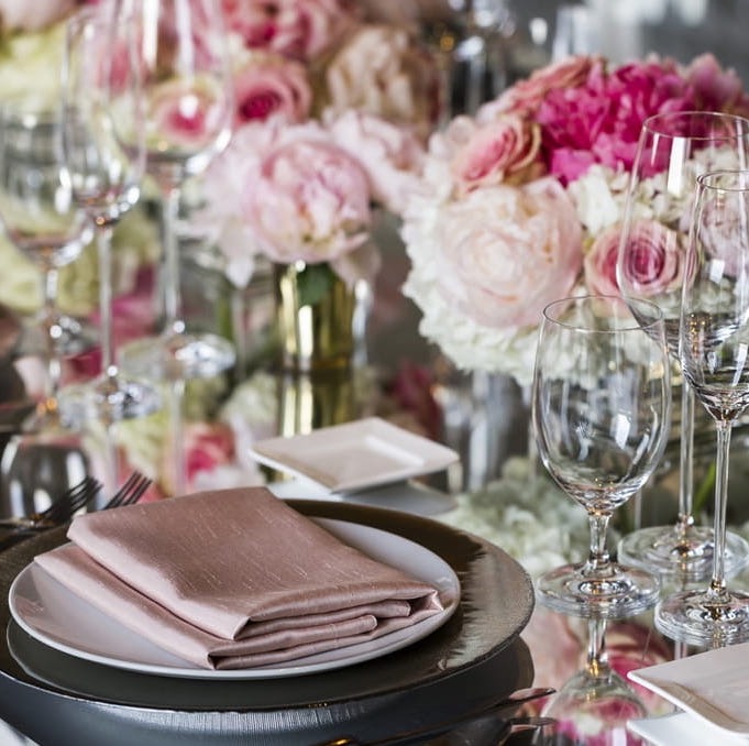 Closeup of ornately set table with lush pink flowers, fine dinner and china, and pink fabric napkin folded neatly