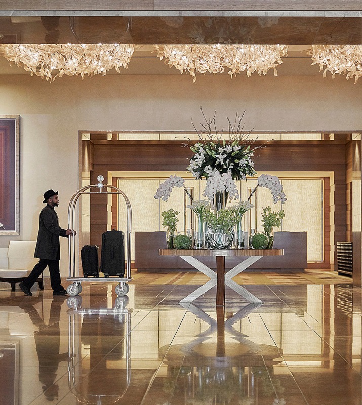 Man with luggage cart walking past the front desk in the Interior lobby of the Four Seasons Hotel in Harbor East