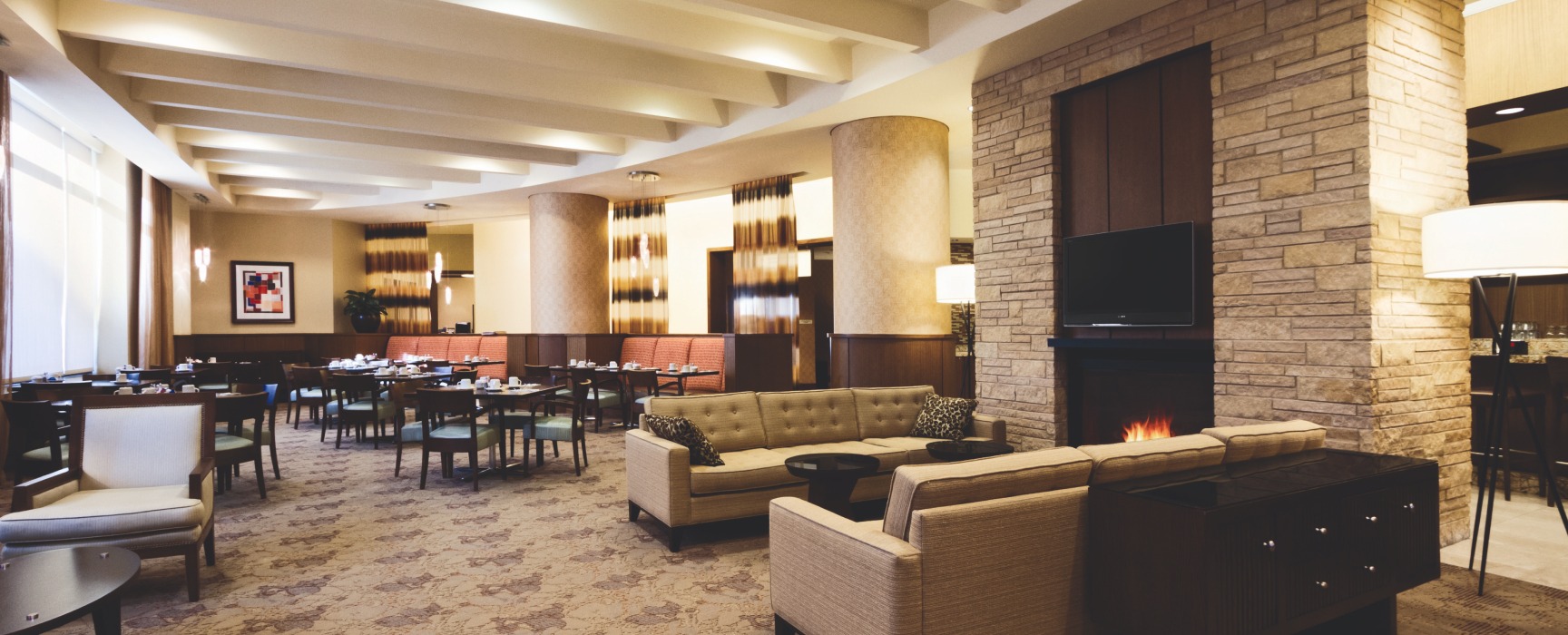 Lobby featuring warm tones and a large fireplace with several cozy sitting areas inside of the Hilton Garden Inn in Harbor East