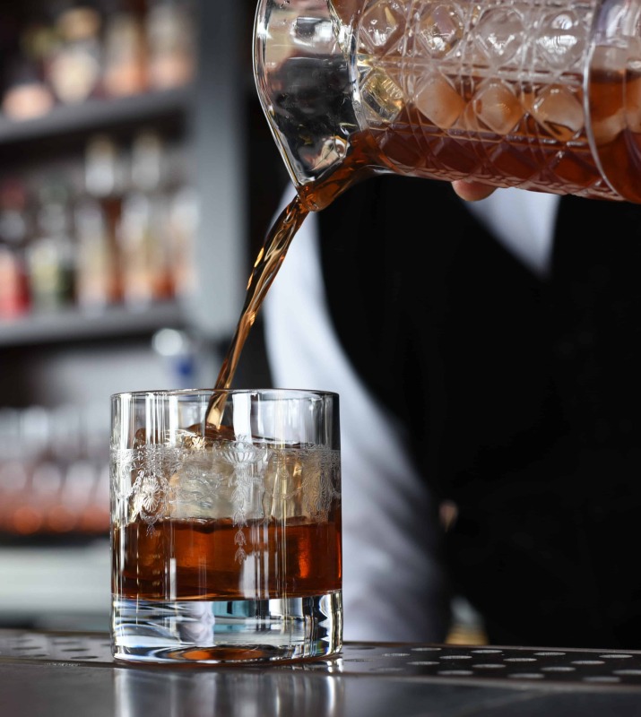 Closeup of bartender pouring brown cocktail into whisky glass