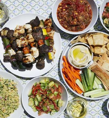 Overhead of various mediterranean appetizers and sides on white plates and patterned table