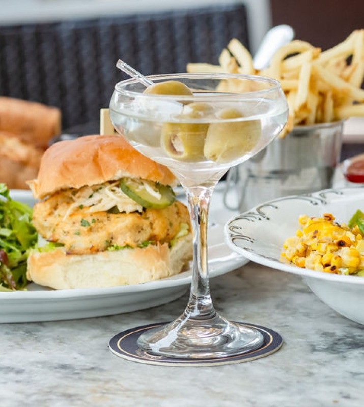 Closeup of martini next to well-plated crab cake sandwich entree and various side dishes