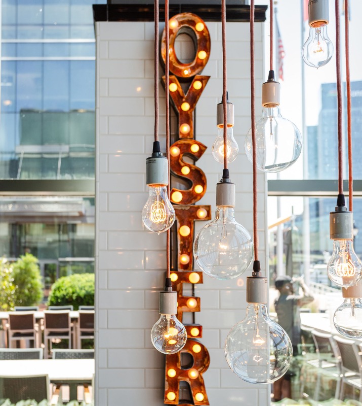Exposed dim hanging lightbulbs in front of large lit-up Oyster sign for Oyster bar