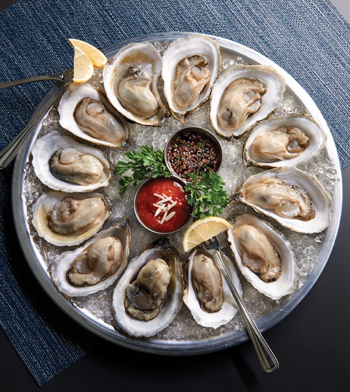 Overhead circle tray of oysters neatly arranged on ice and with sauce and lemon garnishes
