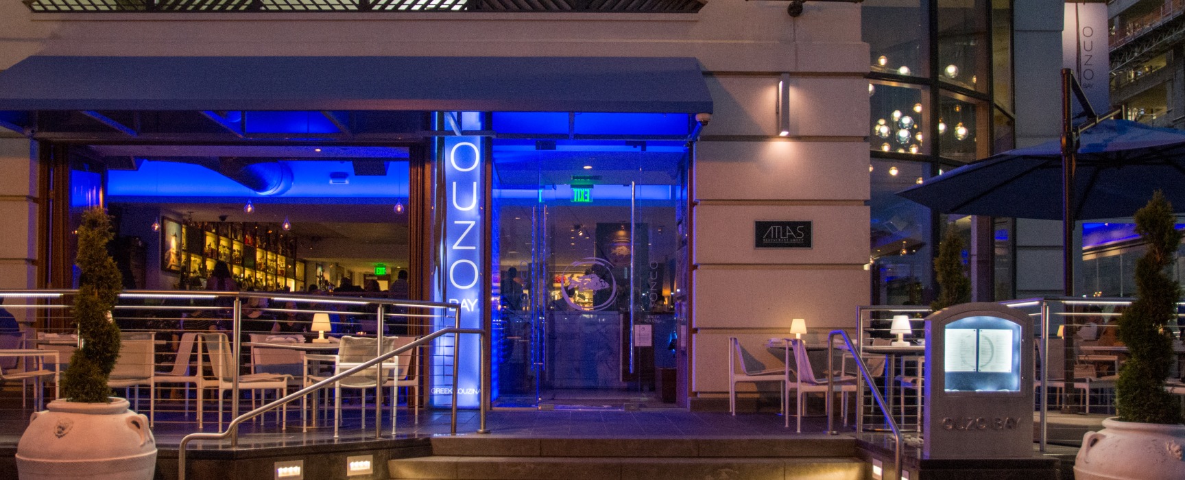 Wide angle nighttime exterior of Ouzo Bay restaurant-front, with inviting blue lighting
