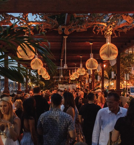 Dimly lit outdoor chic bar packed with people and surrounded by tropical greenery