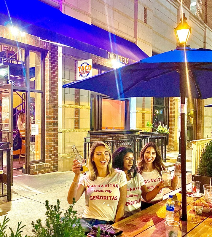 Exterior dining area of Taco Fiesta restaurant featuring blue umbrellas and group of girls cheersing drinks