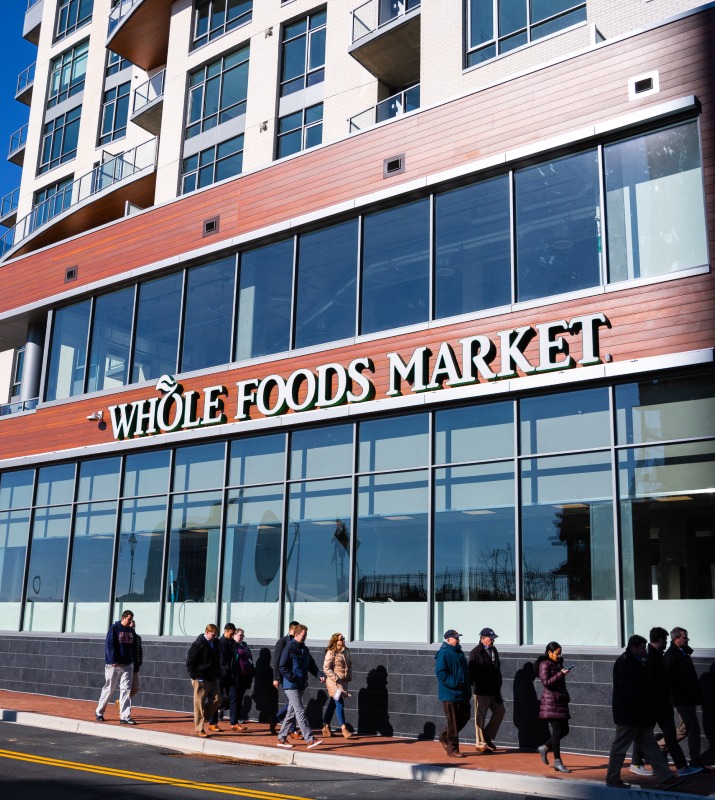 Exterior Whole Foods Market storefront featuring large windows and line of patrons