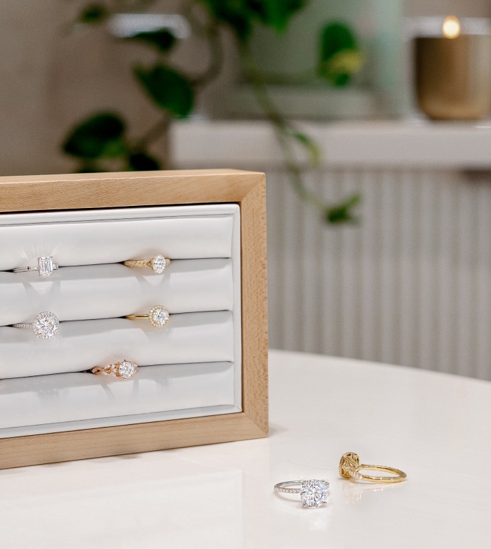 Brilliant Earth diamond engagement rings in upright jewelry holder on white table next to two rings delicately scatted