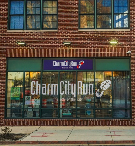 Brick exterior and window of Charm City Run building with white large brand name and footprint logo on windows