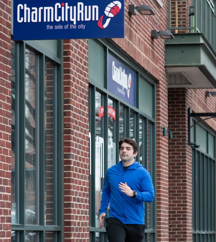 Man in blue running by Charm City Run brick storefront