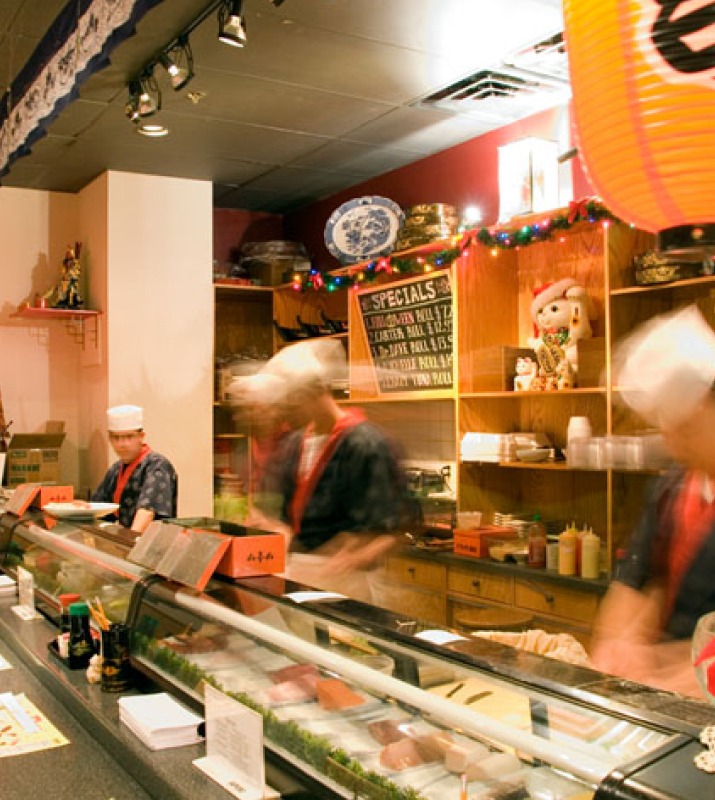 Blurred motion shot of sushi chefs behind sushi counter rolling fish inside of Chiu's Sushi