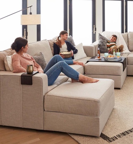 A family of four sits on a large beige couch in an open and airy living room