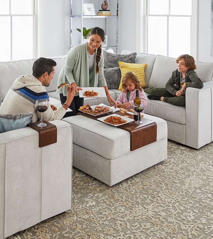 A family of four shares a meal in a bright living room on their gray LoveSac couch