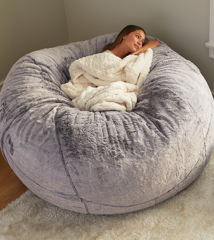 A woman cuddles inside of a large bean bag from LoveSac