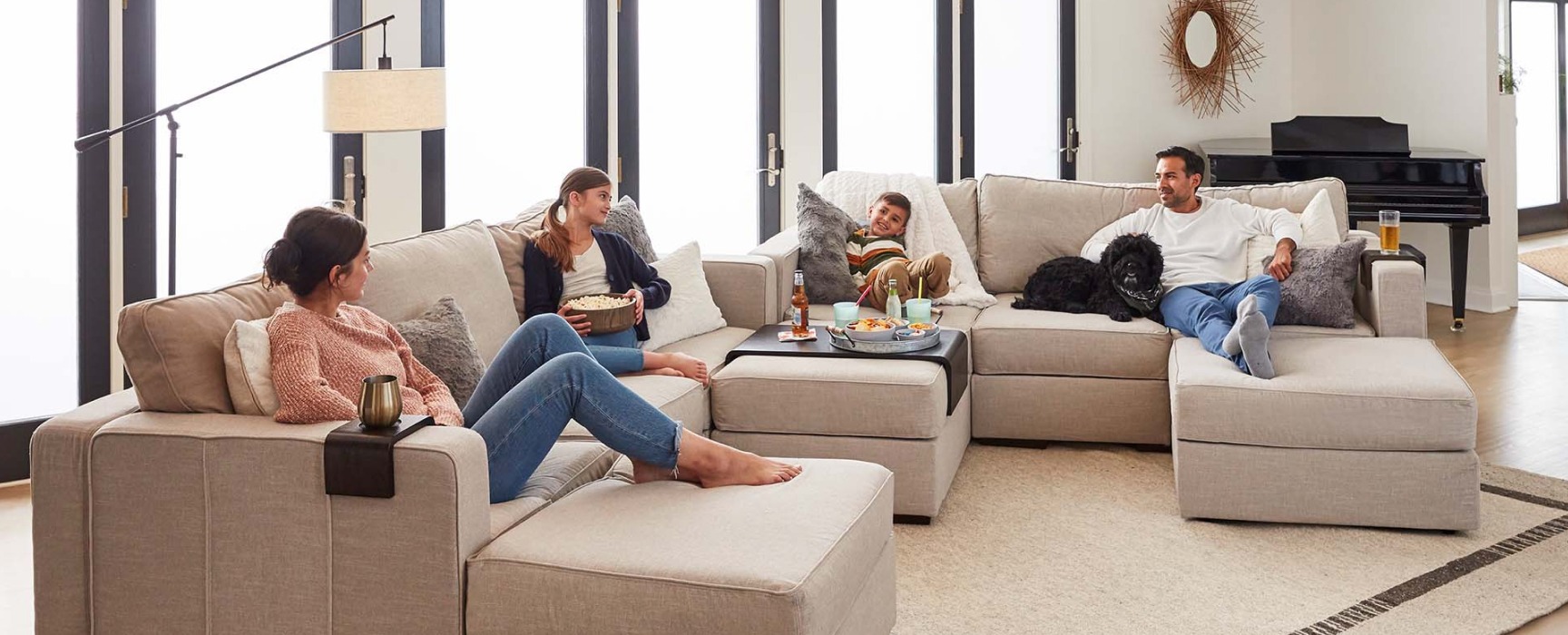 A family of four sits on a large beige couch in an open and airy living room