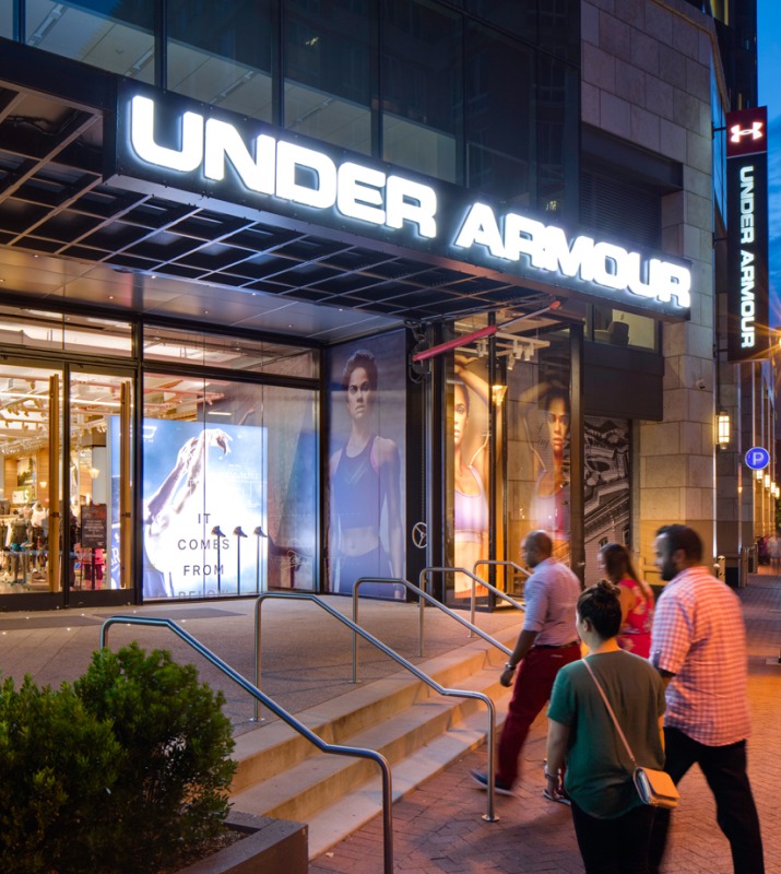 Several people walking into the Under Armour Brand House retail store in Harbor East at dusk