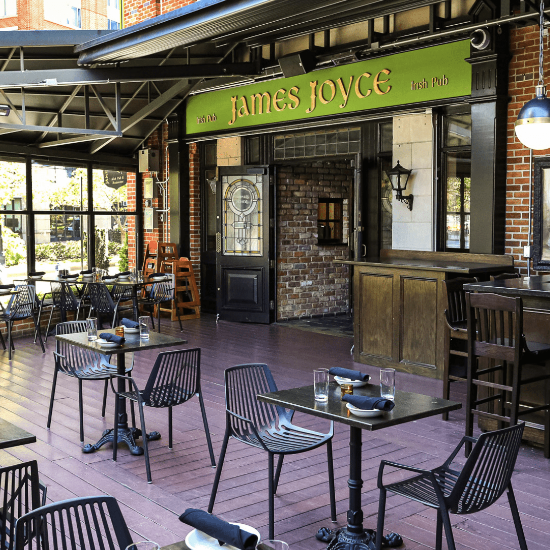 Outdoor dining area of James Joyce Irish Pub featuring dark wooden floors, sleek black chairs, and cozy brick walls