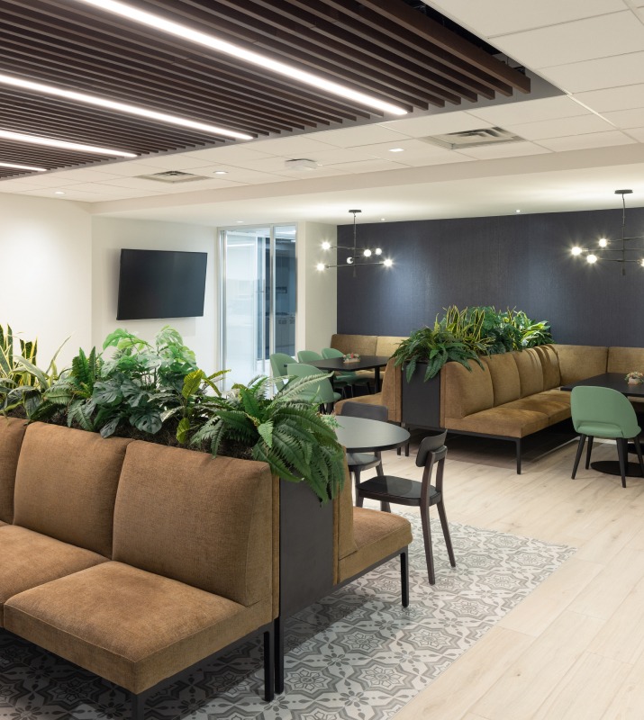 Bench seating and tables surrounded by lush greens and trendy art inside of the 650 S Exeter office building