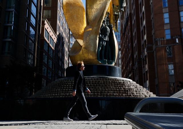Man walking past large gold statue with a fountain in the center of Harbor East