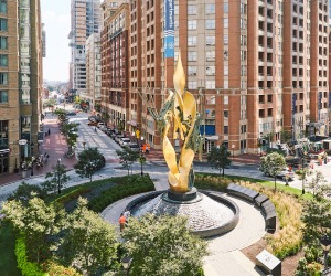 A golden statue with a water feature sits at the center of the circle in Harbor East